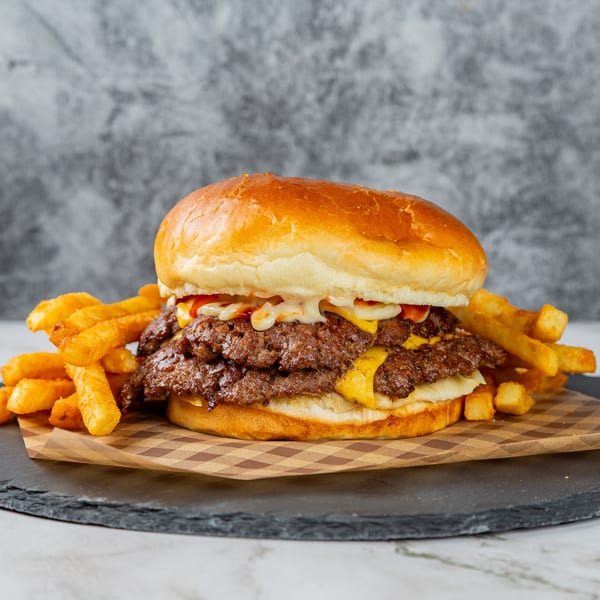 A Rodeo Burgers and Chicken double cheeseburger with fries on a checkered paper and slate board.