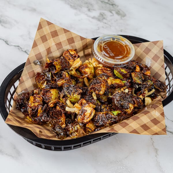 Crispy fried Brussels sprouts with a side of dipping sauce in a black basket lined with checkered paper.