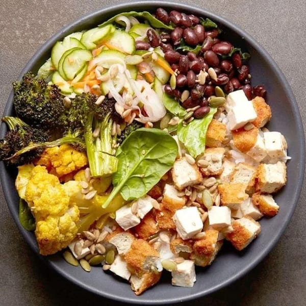 A vibrant Rodeo Burgers and Chicken salad bowl with broccoli, cauliflower, beans, and chicken.
