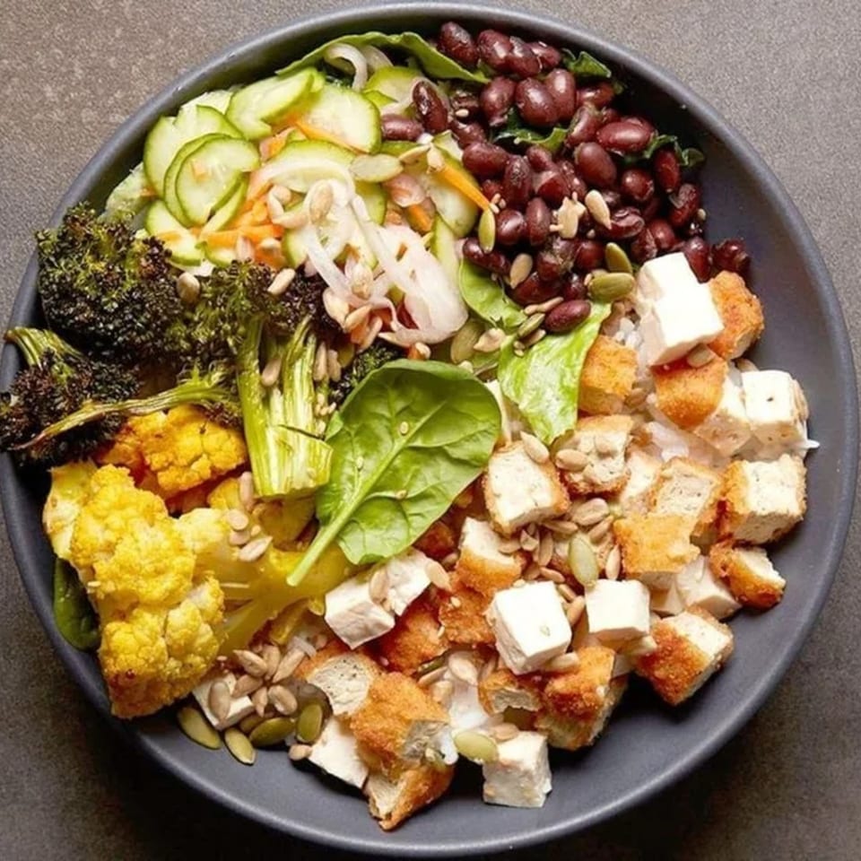 A vibrant Rodeo Burgers and Chicken salad bowl with broccoli, cauliflower, beans, and chicken.