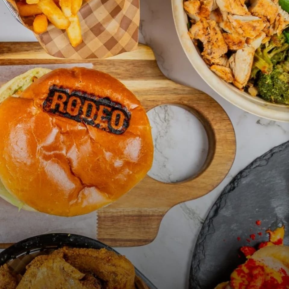Rodeo burger with fries, chicken salad, and fried chicken on a wooden board.