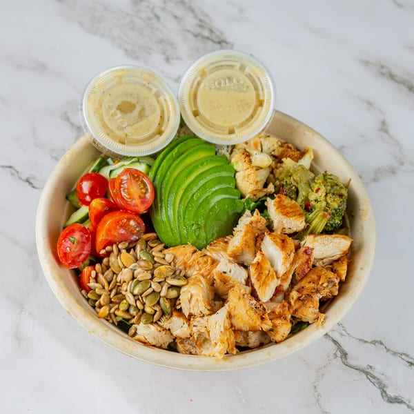 A Rodeo Burgers and Chicken salad bowl with grilled chicken, avocado, tomatoes, seeds, and dressing.