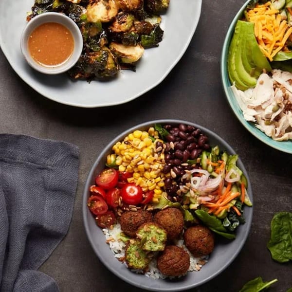 Three bowls of food, including roasted Brussels sprouts, a chicken salad, and a falafel bowl.