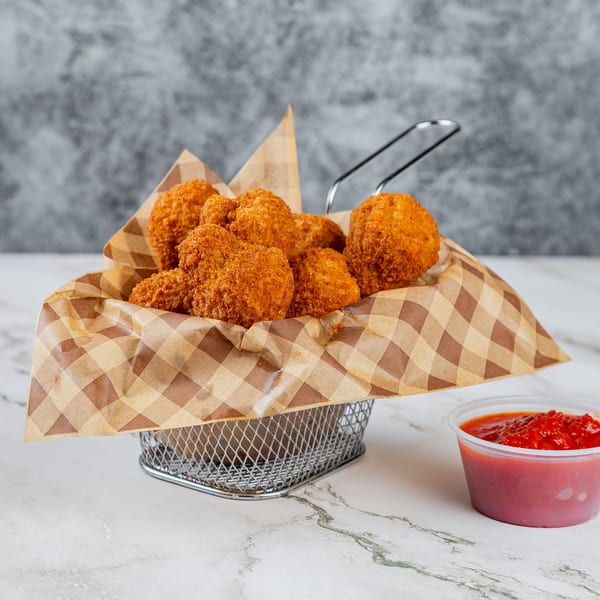 Golden-brown fried chicken bites in a metal basket with checkered paper, alongside a cup of red sauce.