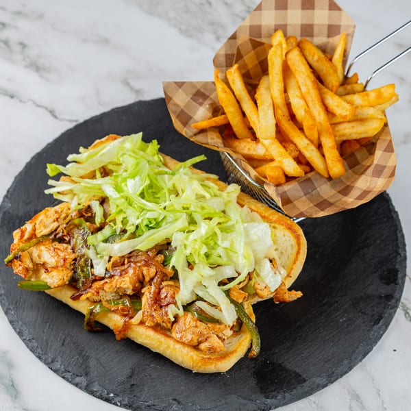 A Rodeo Burgers and Chicken chicken cheesesteak with lettuce, onions, and peppers, served with fries.
